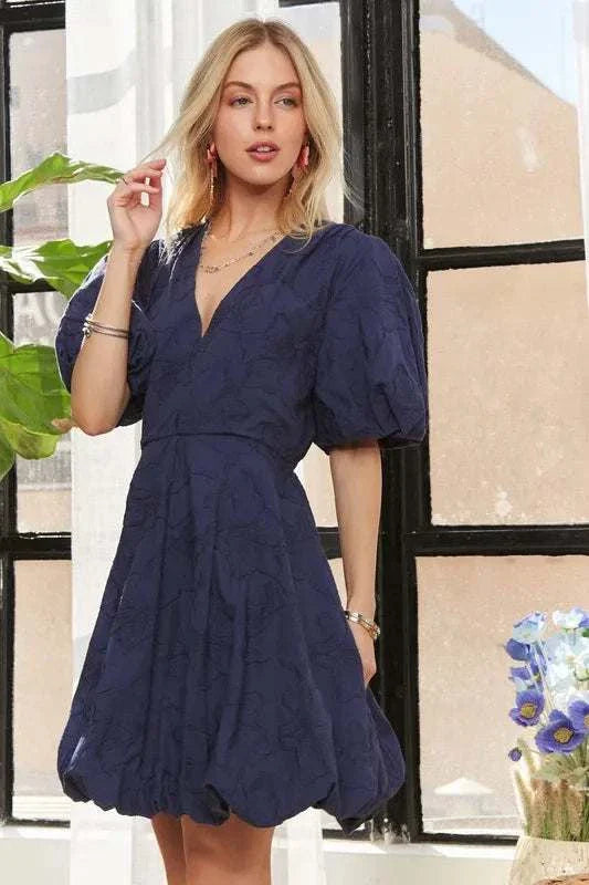 The Indigo Petal DressQuietly romantic and effortlessly polished, The Indigo Petal Dress pairs structured puff sleeves with a softly sculpted mini silhouette. A subtle woven floral texturMini DressesThe Indigo Petal Dress