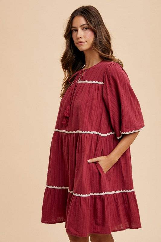 Burgandy Tassel DressEffortless charm in every detail. This breezy tiered dress features delicate contrast trim and a tassel-tie neckline for a touch of boho romance. The rich garnet hueMidi DressesBurgandy Tassel Dress