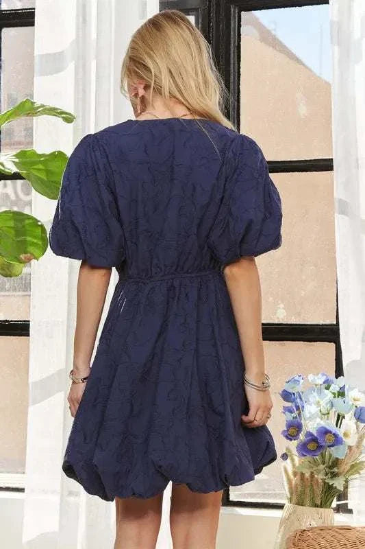 The Indigo Petal DressQuietly romantic and effortlessly polished, The Indigo Petal Dress pairs structured puff sleeves with a softly sculpted mini silhouette. A subtle woven floral texturMini DressesThe Indigo Petal Dress