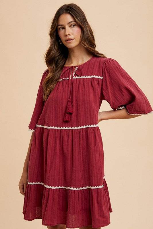 Burgandy Tassel DressEffortless charm in every detail. This breezy tiered dress features delicate contrast trim and a tassel-tie neckline for a touch of boho romance. The rich garnet hueMidi DressesBurgandy Tassel Dress