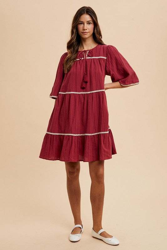 Burgandy Tassel DressEffortless charm in every detail. This breezy tiered dress features delicate contrast trim and a tassel-tie neckline for a touch of boho romance. The rich garnet hueMidi DressesBurgandy Tassel Dress