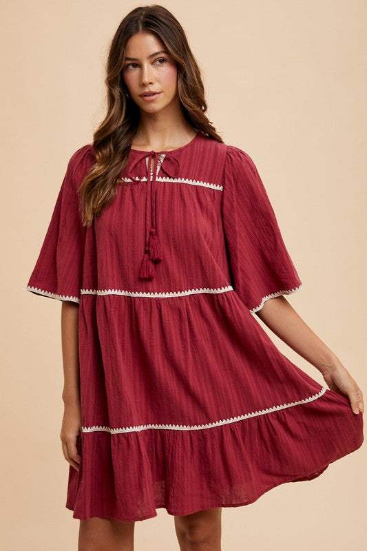 Burgandy Tassel DressEffortless charm in every detail. This breezy tiered dress features delicate contrast trim and a tassel-tie neckline for a touch of boho romance. The rich garnet hueMidi DressesBurgandy Tassel Dress